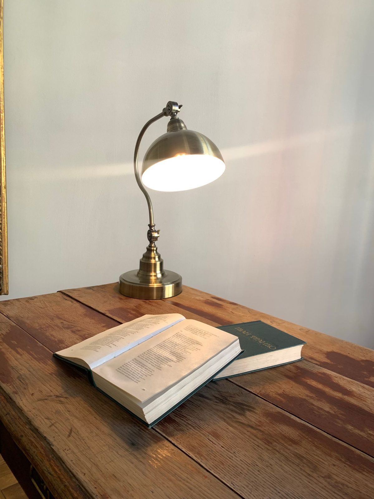 A brass desk lamp lit over an open book on a worn wooden table