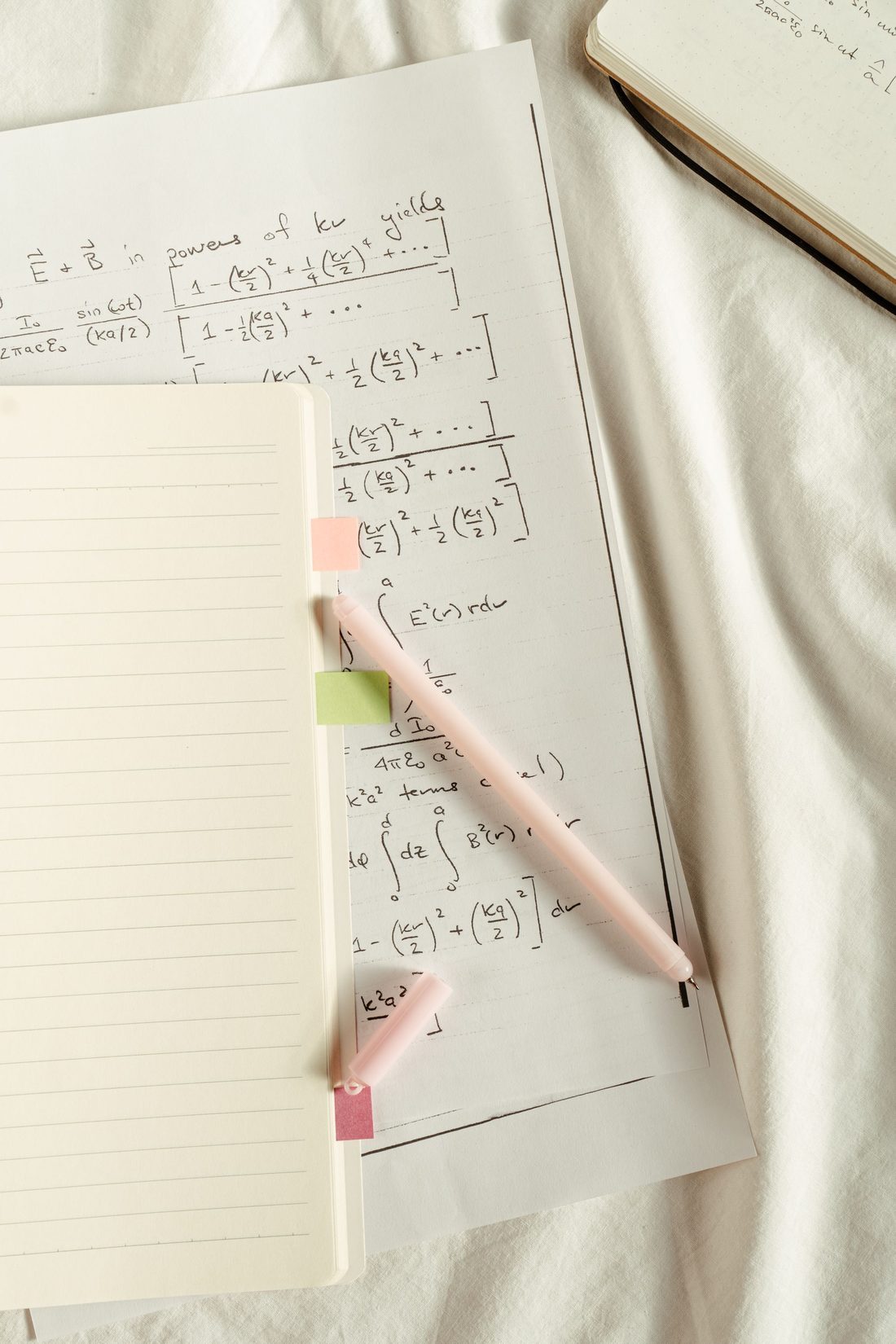 A worksheet of handwritten mathematics beside an open notebook and pen