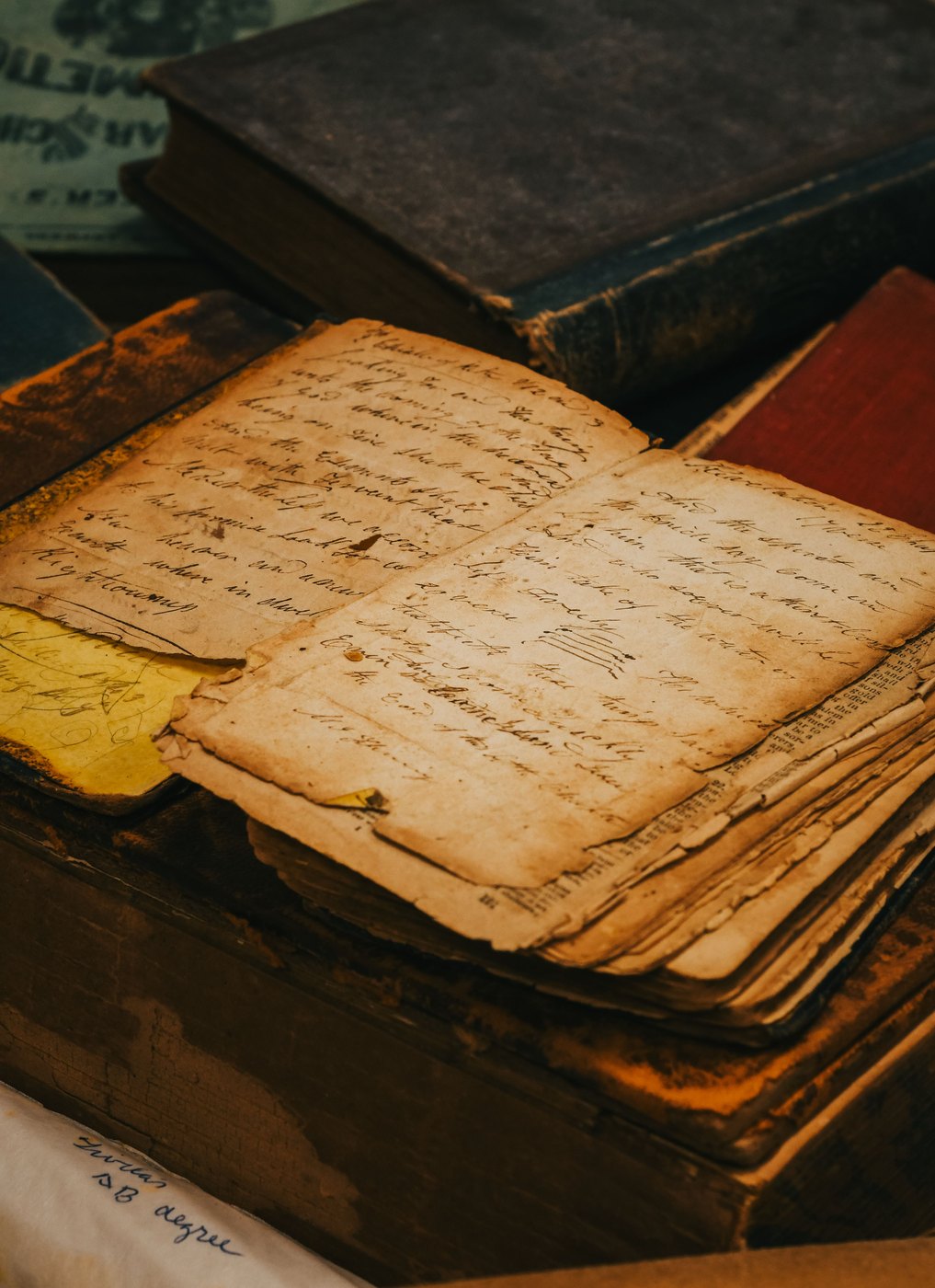 An open handwritten manuscript resting on a stack of worn leather books