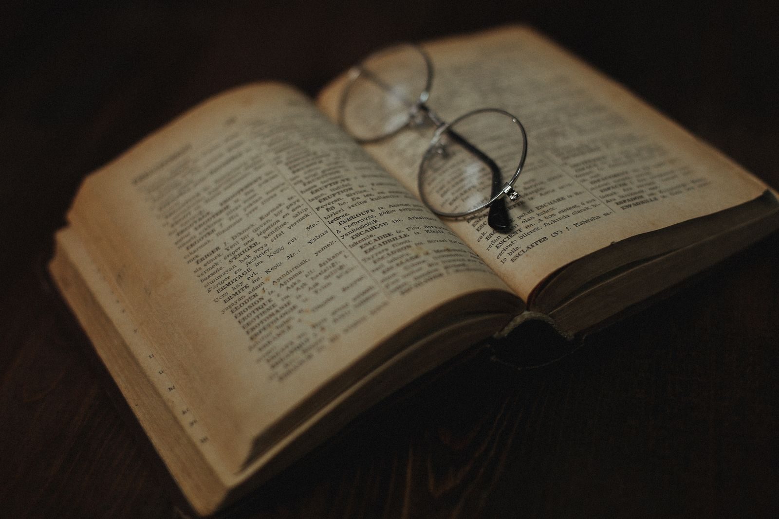 An antique book lying open with a pair of round spectacles resting on its pages